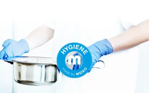 Mani guantate presentano una padella metallica, pronta per essere usata. Il logo MEIKO sottolinea l'igiene.