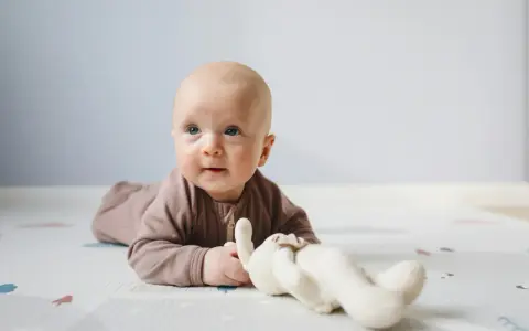 Söt bebis på mage med en mjuk kanin. Bebis mage storlek verkar perfekt för lek och utforskning.