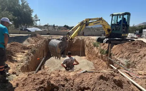Excavadora amarilla trabajando para cavar zanjas en un día soleado. Un hombre supervisa la obra.