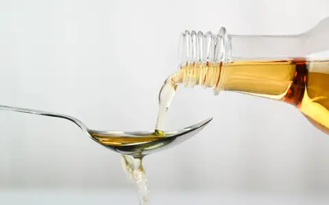 Apfelessig wird aus einer Flasche auf einen Löffel gegossen. Ein Tropfen für das Abnehmen.