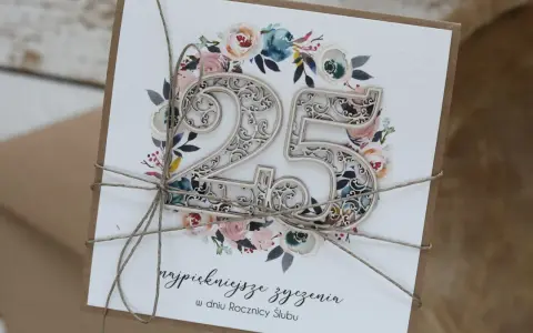 Elegancka kartka z napisem "25 lat małżeństwa jakie to gody", ozdobiona kwiatami i ażurową liczbą 25.