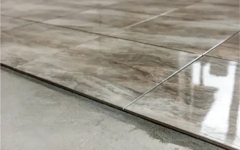 Detalle de las partes de un piso: baldosas de cerámica con veteado marrón y gris, recién colocadas sobre una base de cemento.