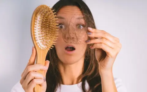 Frau mit erschrockenem Gesicht hält Haarbürste mit Haaren. Hoffnung auf progesteron haare wachsen wieder.