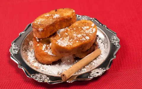 Torrijas de Semana Santa espolvoreadas con azúcar glas y canela, servidas en un plato plateado con una rama de canela.