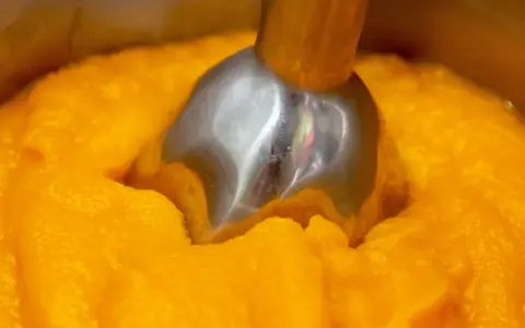 Metalowa końcówka blendera zanurzona w gęstym, pomarańczowym puree z dyni.