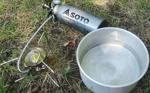 Soto Stormbreaker Kocher mit Brennstoffflasche und Topf auf Gras. Bereit für das nächste Abenteuer.