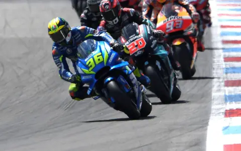 Pilotos de **MotoGP hoy** compiten en una carrera emocionante. El piloto con el número 36 en su Suzuki lidera, inclinado en una curva cerrada.