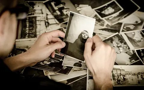 Ręce przeglądają stare fotografie, tworząc osobistą archiwizację zdjęć. Widać portret dziecka i grupowe ujęcia.
