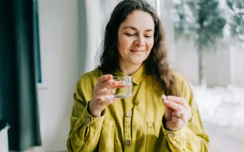 Kvinna med glas vatten och en tablett, funderar på magnesium tillskott biverkningar.