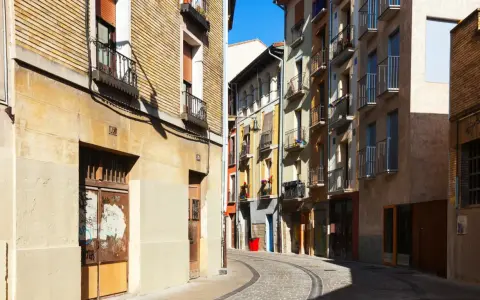 Calle adoquinada con edificios coloridos y balcones. Un cartel de "haya real estate" podría estar en uno de estos locales.