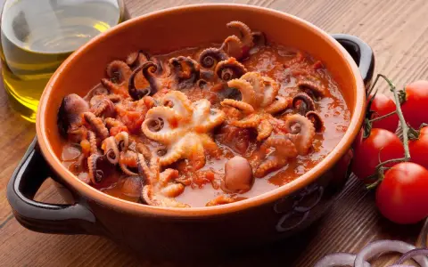 Polipetti in purgatorio, un piatto succulento con tentacoli che danzano in un sugo rosso, accompagnati da pomodorini freschi e cipolla.