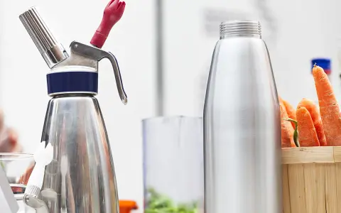 Espuma con sifón lista para crear texturas. Zanahorias frescas al lado, sugiriendo una receta innovadora.
