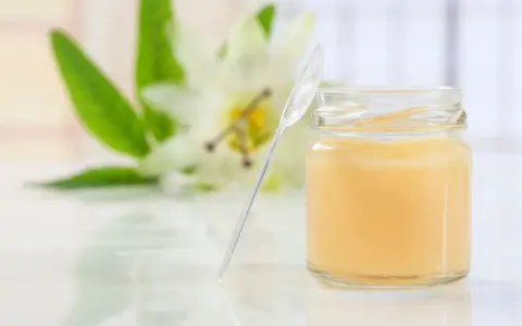 Un vasetto di pappa reale, con un fiore sullo sfondo. Alcuni credono che la pappa reale fa ingrassare, ma è un alimento nutriente.