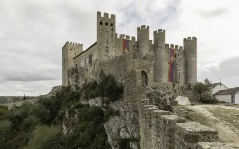 Die Obidos Burg thront majestätisch auf einem Felsen. Fahnen mit dem Namen "Obidos" wehen im Wind.