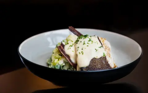 Pyszny lin w śmietanie, podany z puree ziemniaczanym i chrupiącym boczkiem. Danie posypane jest świeżą natką pietruszki.