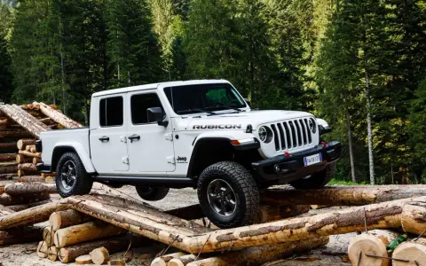 Biały jeep pickup Rubicon pokonuje przeszkodę z bali drewna w lesie.