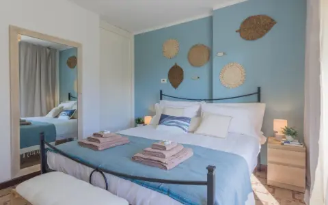 Idee camera da letto: letto matrimoniale con biancheria azzurra e cuscini bianchi, decorazioni a forma di foglia e pesci sulla parete blu.
