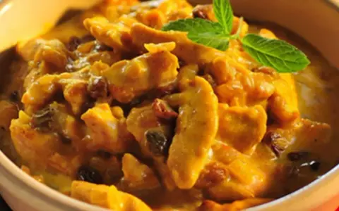 Pyszny kurczak w sosie curry z rodzynkami, ozdobiony listkiem mięty. Idealny przykład, jak zrobić sos curry do kurczaka.