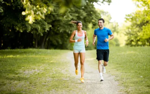 Ein lachendes Paar joggt glücklich durch einen sonnigen Park. Sie genießen die frische Luft und die Bewegung – das ist, was Joggen bringt.