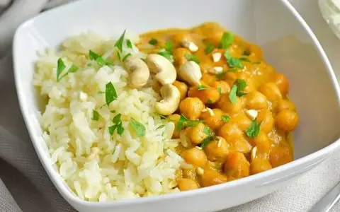 Curry de garbanzos cremoso con arroz blanco y anacardos en un cuenco blanco.