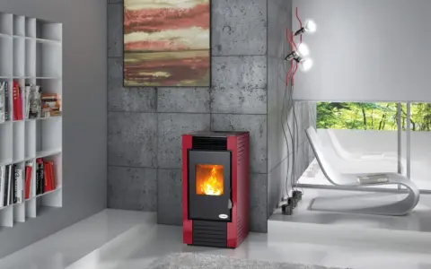 Estufa roja moderna con fuego encendido, mostrando cómo funciona la biomasa. Estantería blanca con libros y sillones blancos al fondo.