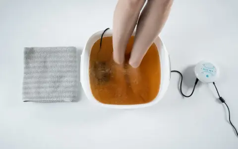 A person's feet are soaking in a foot spa with a brown solution, suggesting a method for how to remove toxins from feet naturally. A towel is nearby.