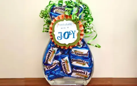 Un jarrón lleno de botes de chuches caseros, decorado con un lazo verde y un mensaje que dice "BIRTHDAYS are a JOY".