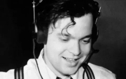 Orson Welles, giovane e sorridente con cuffie, un'immagine che evoca la sua genialità, ma non il suo orson welles causa morte.