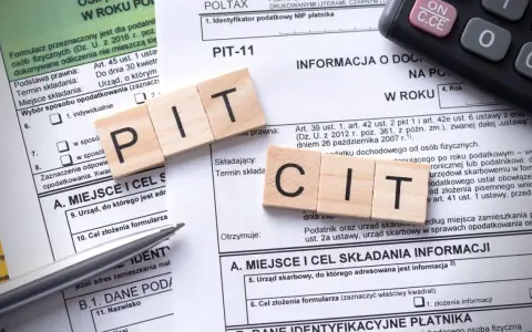 Drewniane klocki z literami "PIT" i "CIT" na formularzu podatkowym. Temat: podatek od sprzedaży nieruchomości po upływie 5 lat.