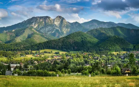 Malowniczy widok na Tatry z Jaszczurówki, gdzie liczne atrakcje czekają na turystów. Zielone wzgórza i tradycyjna zabudowa tworzą sielski krajobraz.