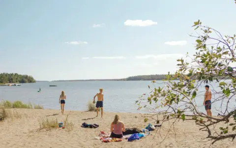 Solig dag vid Hallmare havsbad. Människor njuter på stranden, badar och leker i vattnet.