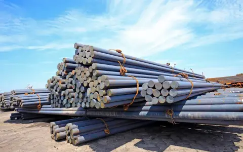 Stapel von Metallstäben, die den Unterschied zwischen Eisen und Stahl veranschaulichen. Sie liegen unter blauem Himmel.