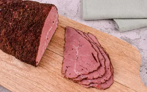 Pastrami co to? Aromatyczny, peklowany i wędzony kawałek wołowiny, pokrojony w cienkie plastry, leżący na desce.