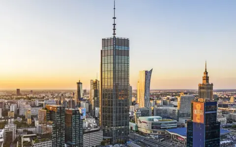 Warszawski krajobraz zdominowany przez wieżowce, w tym najwyższy hotel w Warszawie, lśni w złotym świetle zachodzącego słońca.