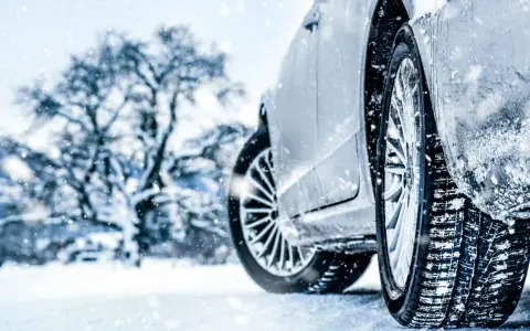 Auto im Schnee mit Winterreifen, verschneiter Baum im Hintergrund.