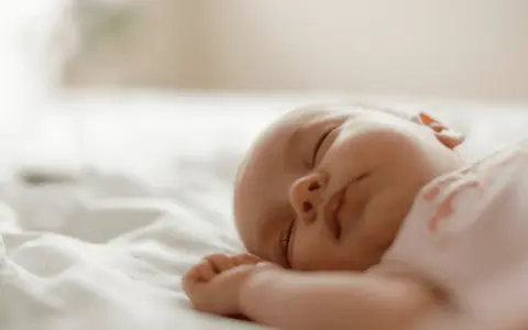 Śpiące niemowlę na białej pościeli.