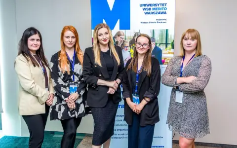 Pięć kobiet pozuje przed banerem Uniwersytetu WSB Merito Warszawa. To zespół, który tworzy wspaniałą wsb praca.