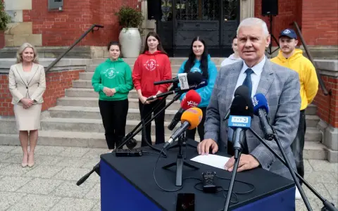 Konferencja prasowa z udziałem studentów filologii norweskiej zaocznie. Mężczyzna w garniturze przemawia do mikrofonów.