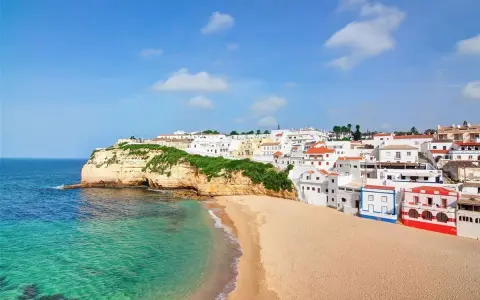 Traumhafte Küstenlandschaft in Portugal, Carvoeiro: Weiße Häuser schmiegen sich an grüne Klippen, daneben ein goldener Sandstrand und türkisfarbenes Meer.