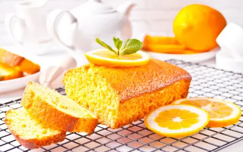 Un soffice plumcake al limone, guarnito con una fetta d'arancia e menta, su una griglia, pronto per essere gustato.