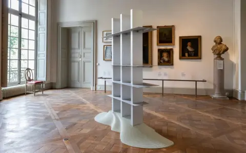 En modern skulptur, som en hyllning till Gustav Winsth, står i ett rum med gamla målningar och en byst.