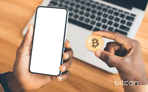 Dłoń trzyma smartfon z pustym ekranem i monetę bitcoin. Możliwe, że to początek przygody z kopanie kryptowalut na telefonie.