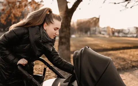 Mama przygotowuje malucha na spacer w 15 stopniach. Ciepła kurtka i szalik to podstawa, by zapewnić komfort dziecku w wózku.