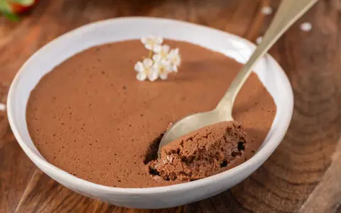 Une cuillère prend une bouchée d'une mousse au chocolat facile et aérienne, garnie de petites fleurs blanches.