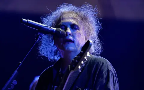 Robert Smith, en av medlemmar av The Cure, sjunger vid en mikrofon med sitt karaktäristiska hår.