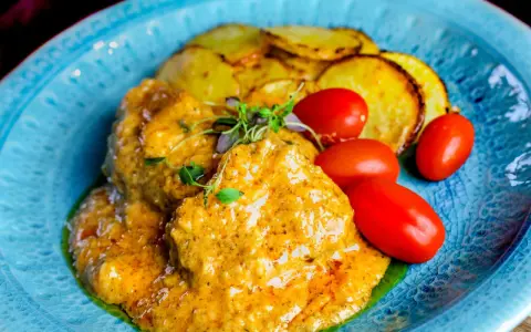 Köttbullar i krämig cafe de paris sås med rostade potatisskivor och körsbärstomater på en blå tallrik.
