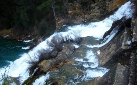 El salto de Poveda, una cascada de agua blanca y espumosa que desciende por rocas y vegetación, desemboca en un río de aguas turquesas.