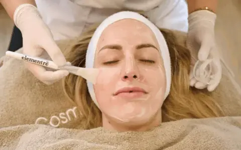 Kosmetikerin trägt eine Maske auf, um die Haut zu reinigen.