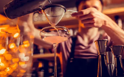 Un barman verse un cocktail d'un shaker dans un verre. C'est ainsi qu'un shaker sert à mélanger et refroidir les boissons.