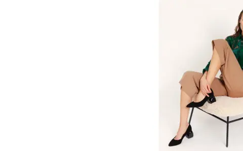Eleganckie czarne czółenka na geometrycznym obcasie to idealne buty na jesień. Modelka prezentuje je w stylizacji z beżowymi spodniami i zieloną bluzką.